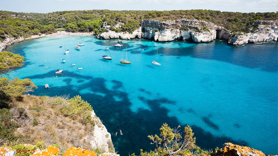 Cala Macarella, a bay with anchored sailboats and turquoise water
