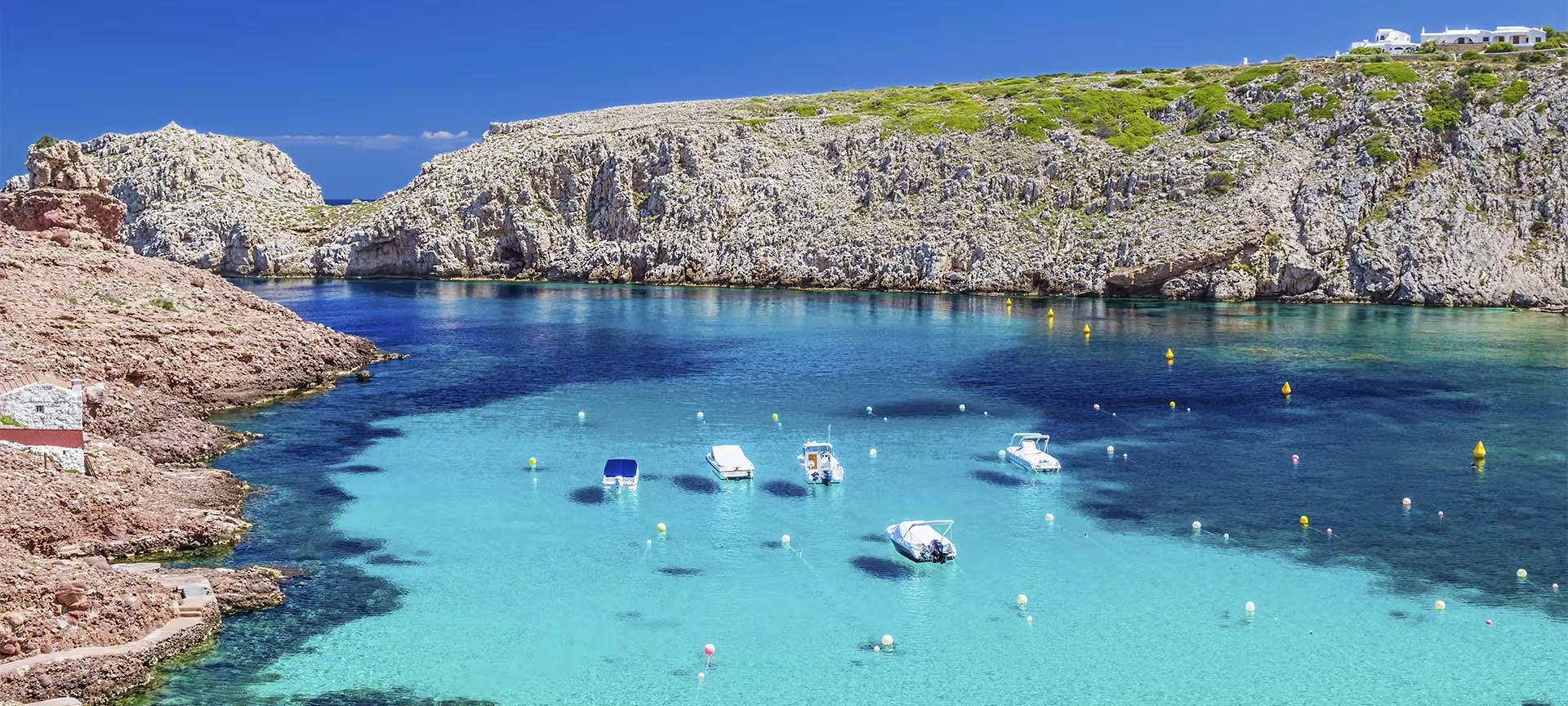 Rocky cove of clear turquoise water with boats moored, ringed by unspoiled cliffs