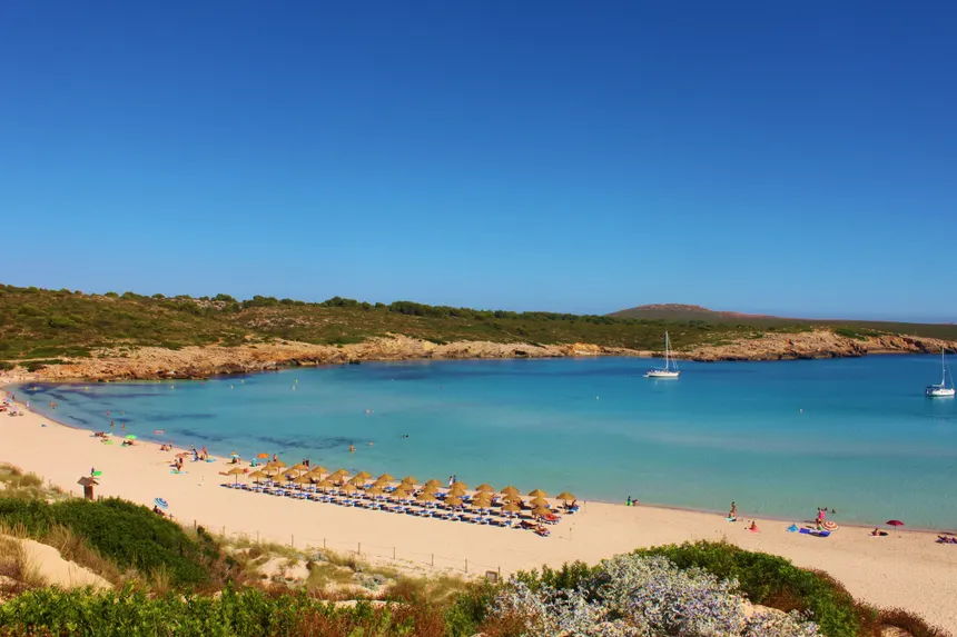 Son Saura Beach, a wide crescent of white sand and turquoise water backed by pines