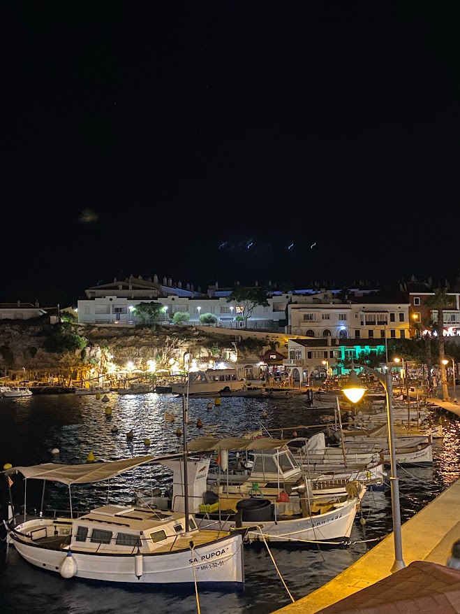 Cales Fonts harbour at night, boats moored along the lit shoreline