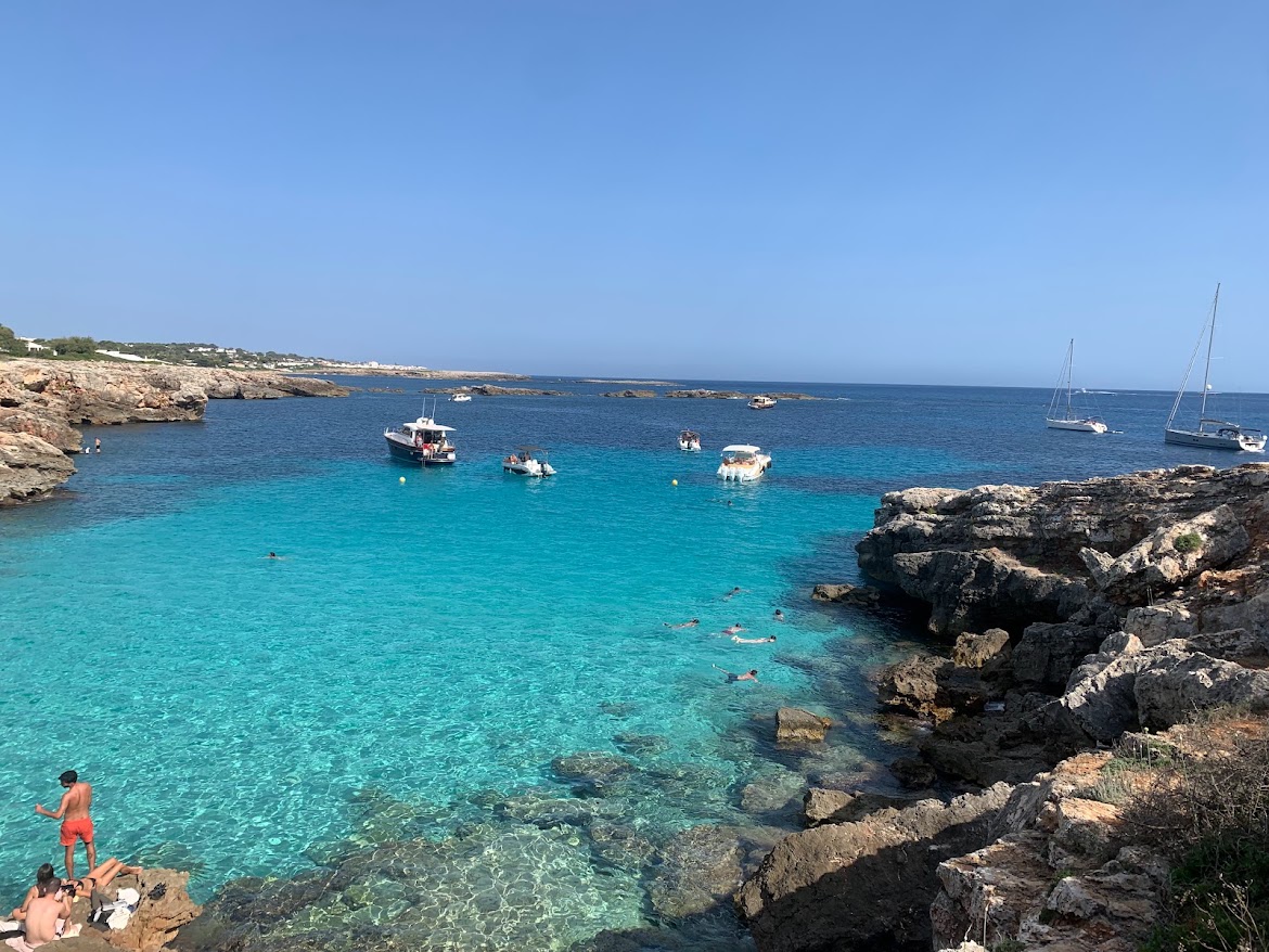 Turquoise cove with boats moored, seen from the rocks