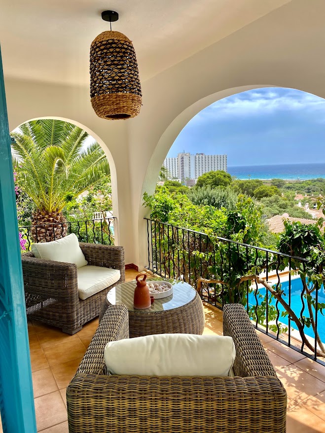 Covered terrace with wicker chairs overlooking the pool and sea